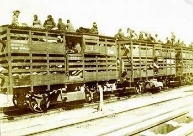 Υπόμνημα: 1915 – Εκτοπισμένοι Αρμένιοι σε βαγόνια μεταφοράς ζώων στη σιδηροδρομική γραμμή που ονομάζεται «Βερολίνο-Βαγδάτη» και κατασκευάστηκε στην Οθωμανική Αυτοκρατορία από την γερμανική εταιρεία «Kompany Bahn». Απ’ αυτή την ονομασία προέρχεται το όνομα της πόλης Kobanê (Ayn al-Arab), που ιδρύθηκε από τους επιζώντες της γενοκτονίας των Αρμενίων το 1915 κατόπιν εντολής της κυβέρνησης των Νεοτούρκων